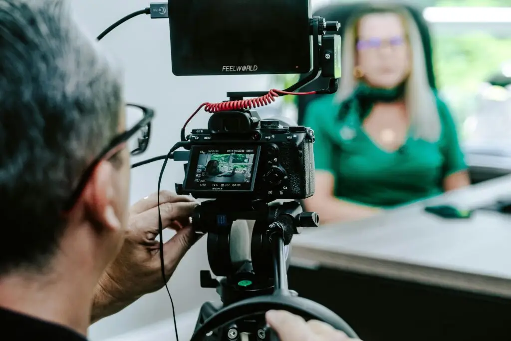 Close-up of a videographer filming a woman in an office setting, highlighting professional equipment.